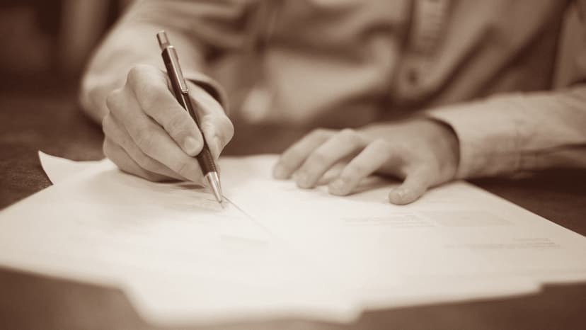 Mano che scrive su un foglio con calcolatrice e computer portatile